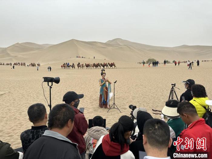 圖為2023年4月底，敦煌大漠“逐舞者”奧楠在鳴沙山月牙泉景區(qū)視頻直播，吸引游人圍觀。　馮志軍 攝